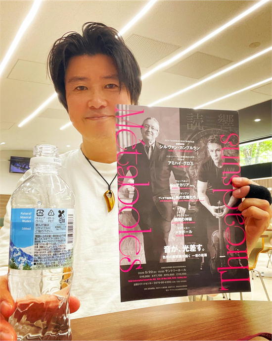 読響のコンサートフライヤーを持つ斉藤浩。右手にペットボトルを持ち、フライヤーにはシルヴァン・カンブルランの写真と「音が、光差す。」の文字が見える。